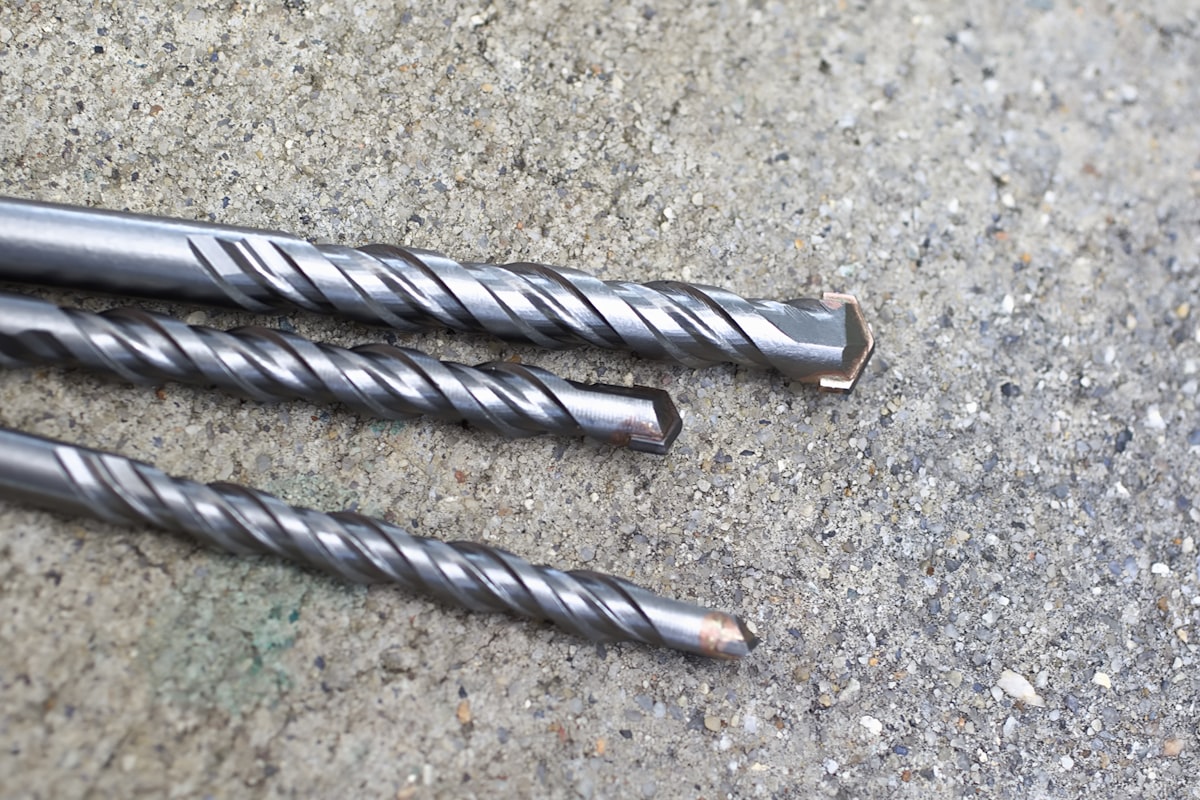 Three metal drill bits standing upright on a concrete surface