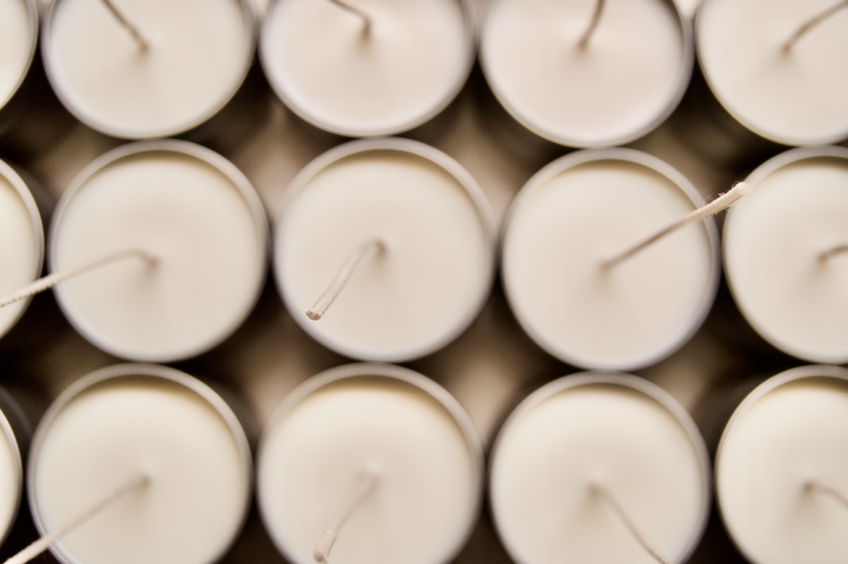 Candle making supplies including soy wax, wicks, fragrance oils, and handmade candles on a wooden workbench