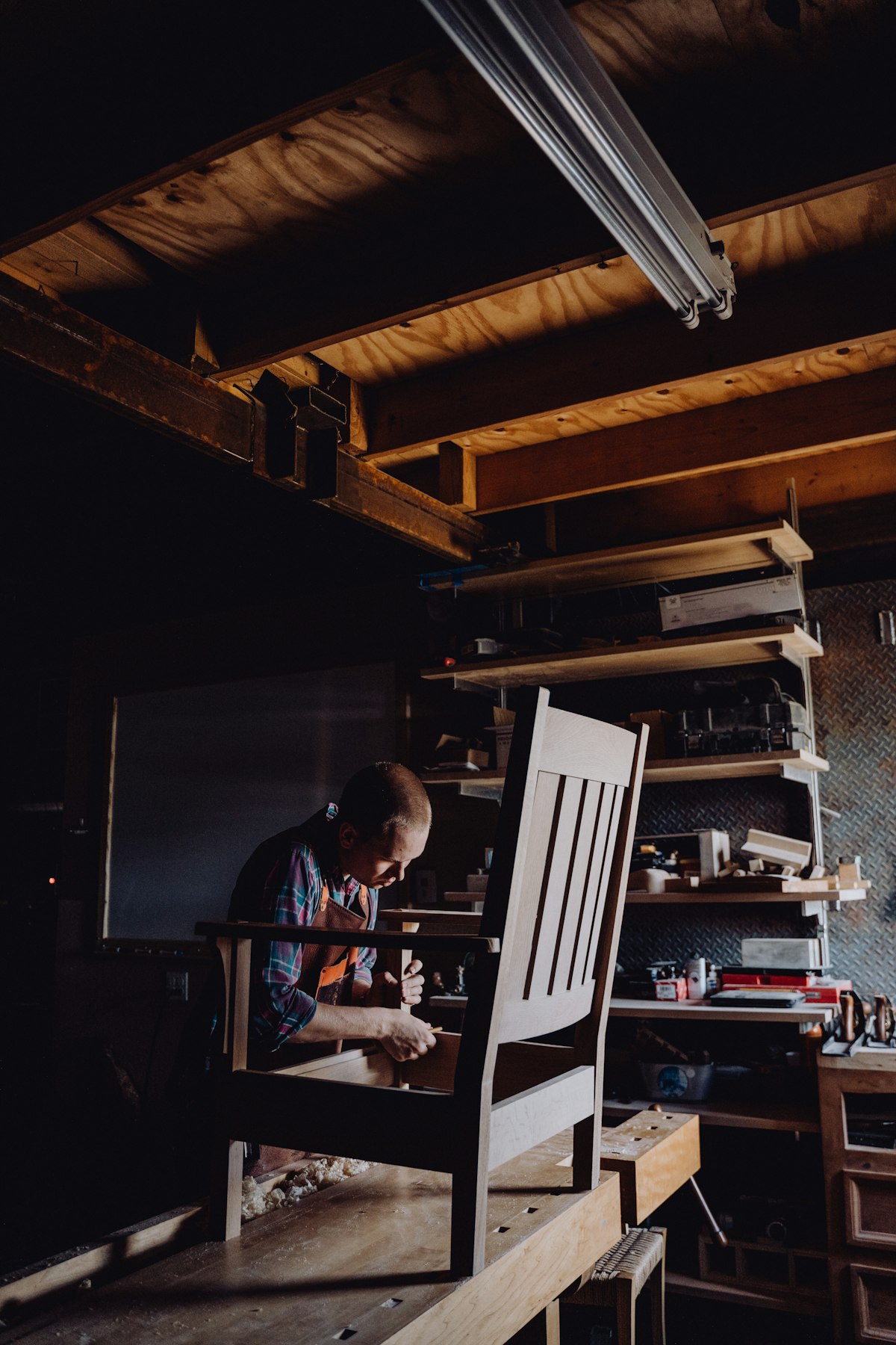 Craftsman sanding a wooden chair in a workshop, with wood sheet material nearby