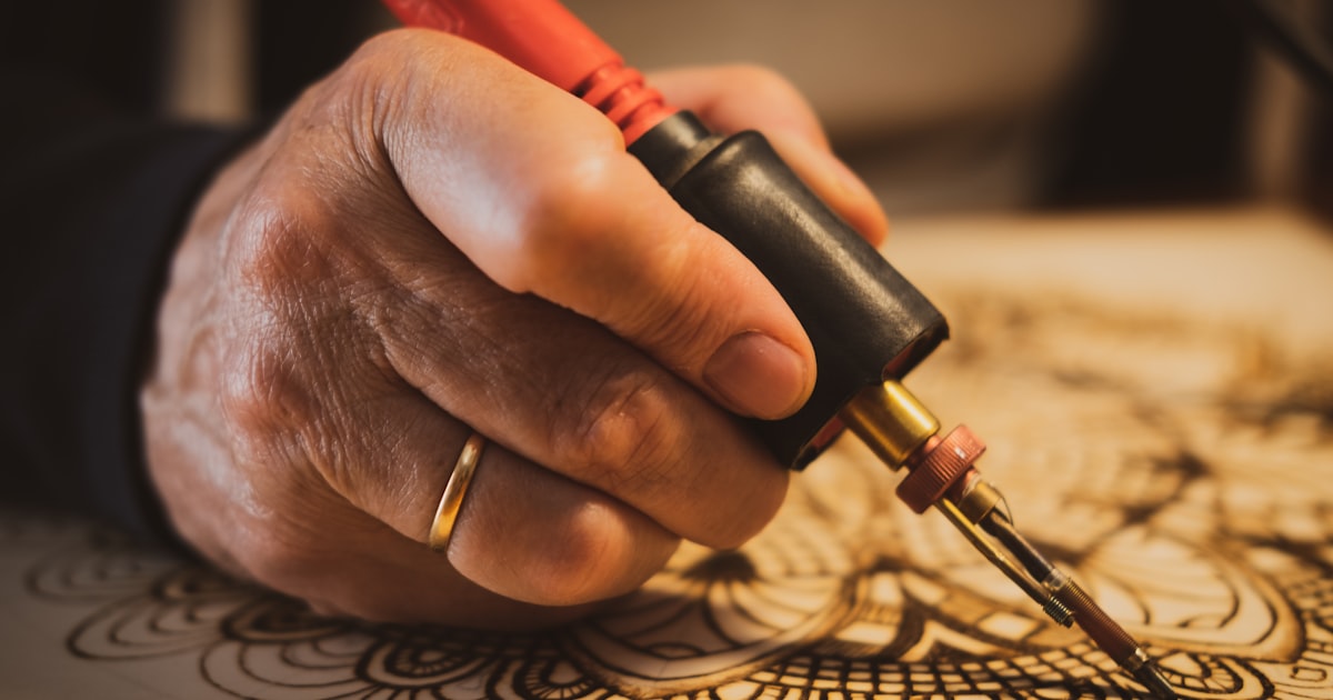 Pyrography pen burning a detailed mandala design into a wooden board